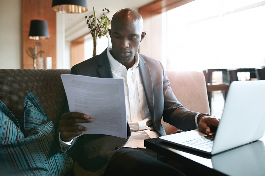 Man in a business suit working at a laptop and reading a document.